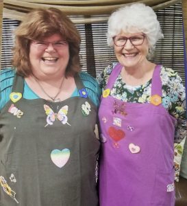 Annette Teepe and Pam Ray wearing big smiles and their story aprons