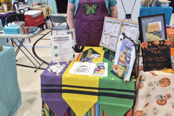 Author at vendor table with coloring book bundles and colorful table decorations at the Faith Cumberland Fall Festival.
